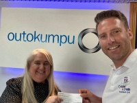 Staff at Outokumpu presenting cheque in front of an illuminated Outokumpu sign